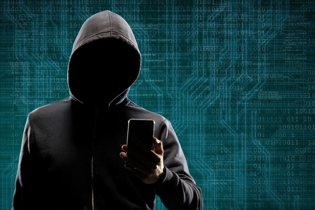 A computer hacker wearing a black hoodie while using a phone in front of a digital background