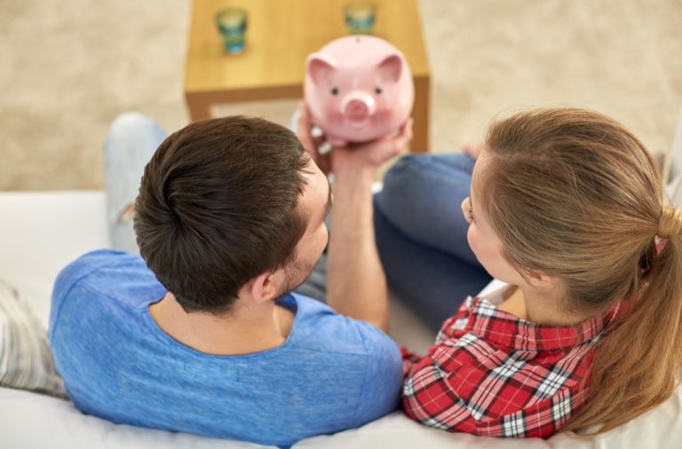 Concept of tight financing. A couple looking into opening their piggy bank while seated on a sofa